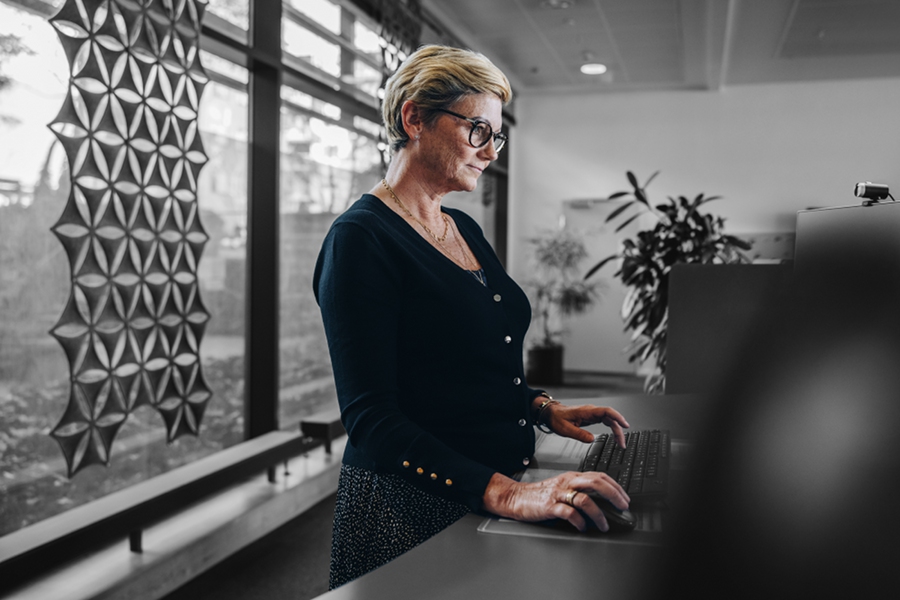 Senior businesswoman working at standing desk. Woman employee working on desktop computer at ergonomic standing desk.