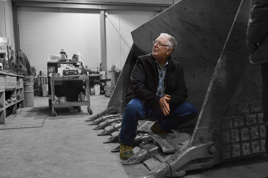 a man crouches in the bucket of a front loader in a warehouse