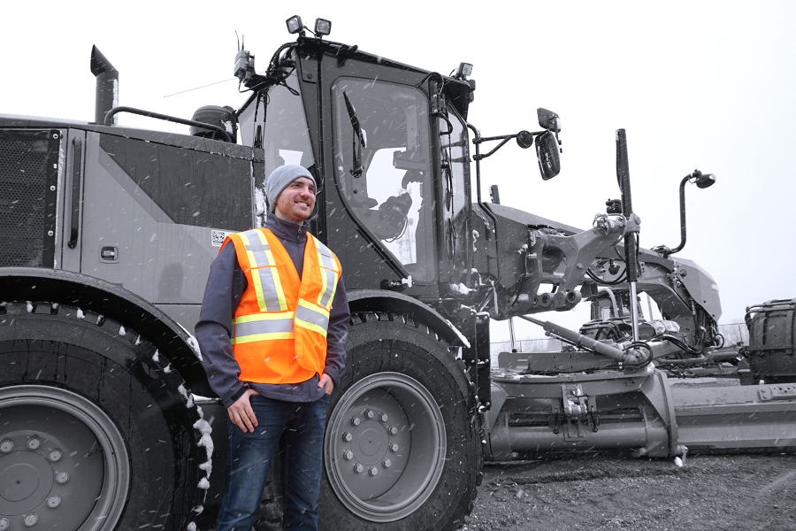 a man in safety gear stands in front of a grader