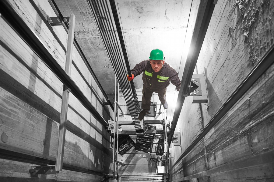 lift machinist worker adjusting elevator mechanism in elevator shaft hoistway