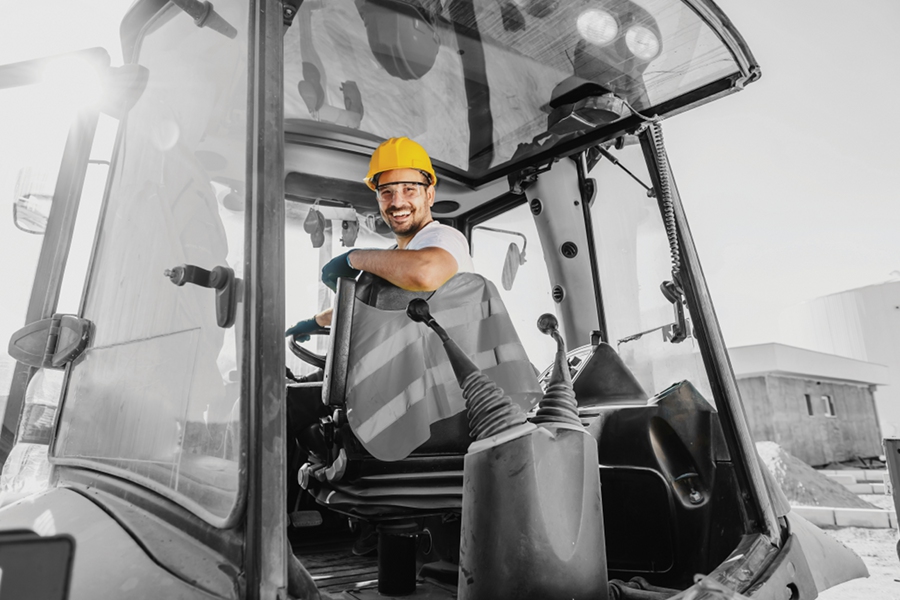 Smiling worker with helmet driving an excavator