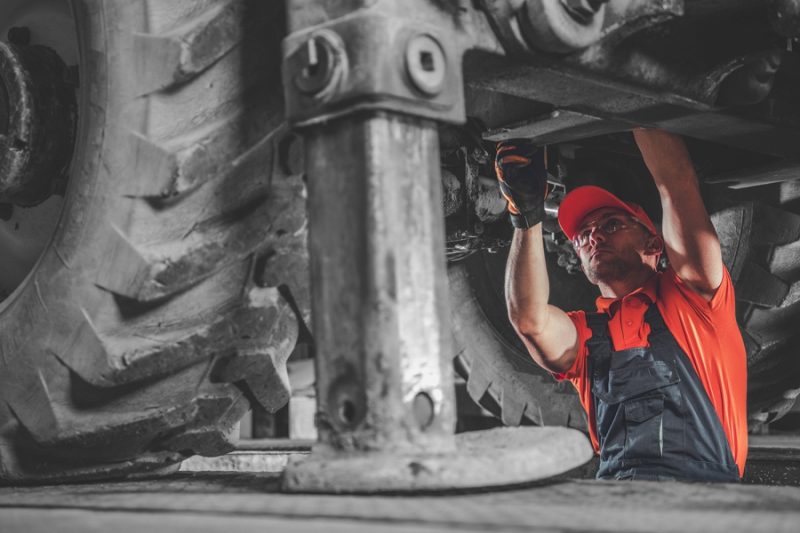 Small Excavator Repair and Maintenance. Caucasian Heavy Equipment Mechanic Trying to Find an Issue. Industrial Theme.