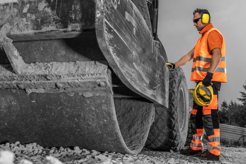 a man in safety gear stands next to a paving machine