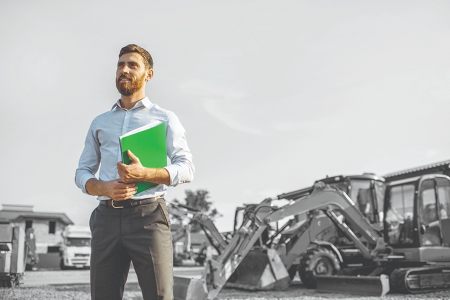 a man with a clipboard stands in front of a lot of machinery up for auction