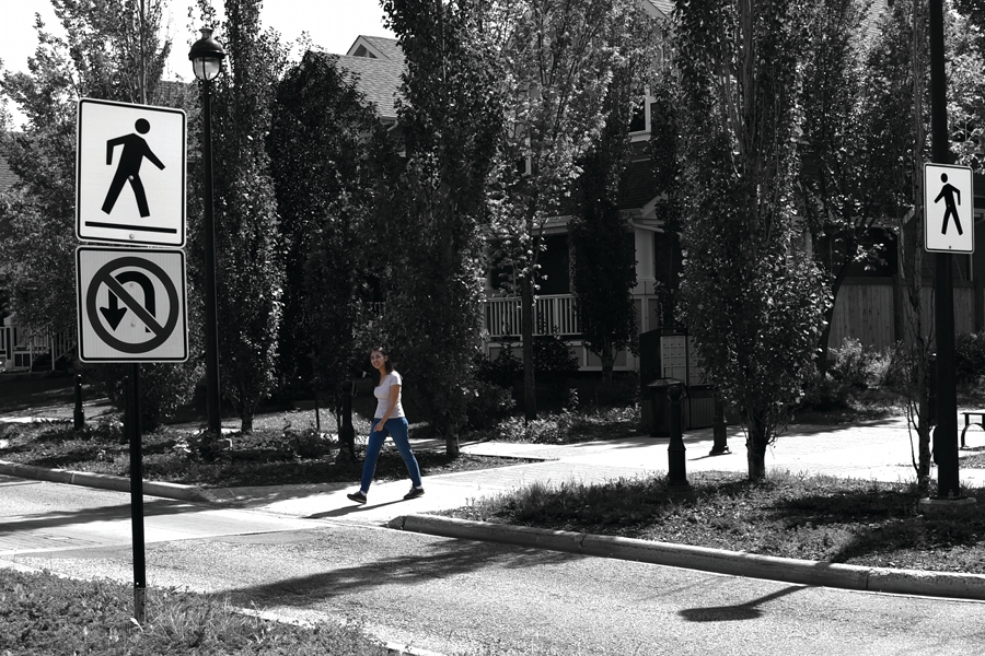 A woman crosses the street via a crosswalk marked by signs