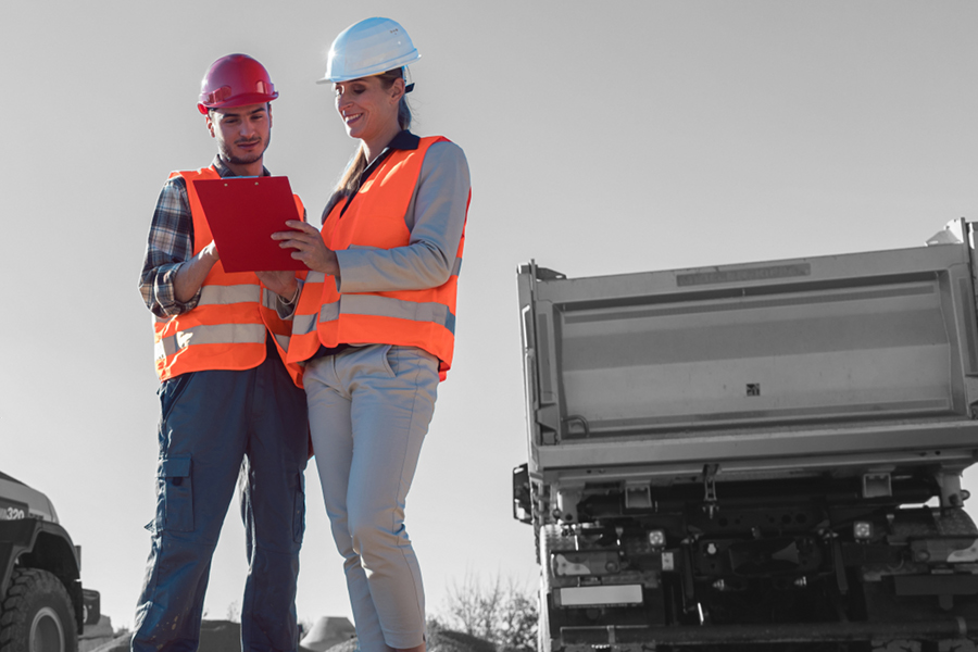 two workers discussing the contents of a clipboard near a truck hauling gravel