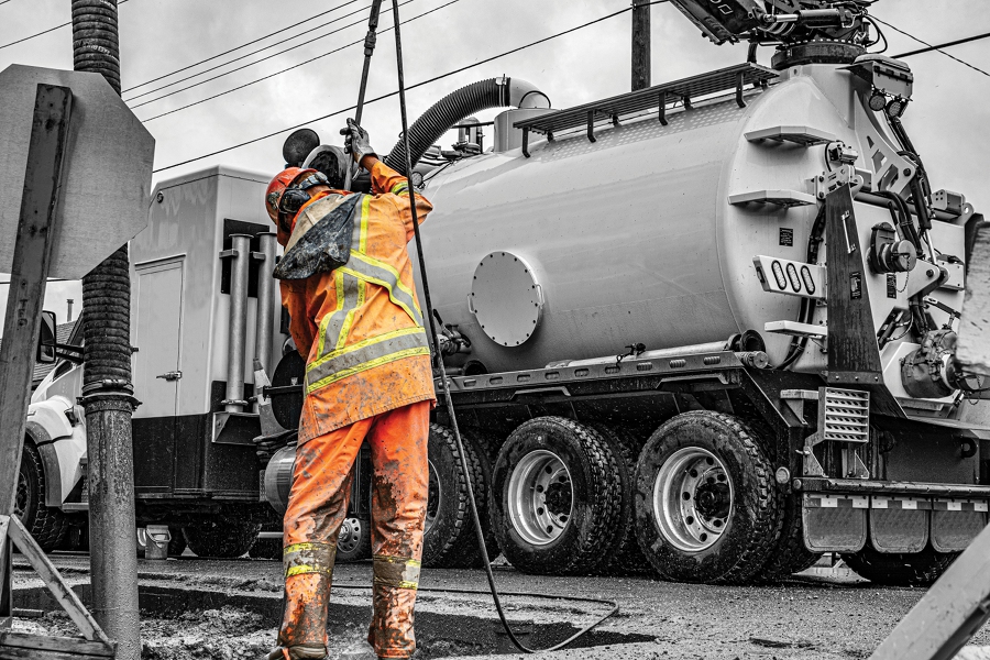 a worker in safety equipment stands next to a vacuum truck