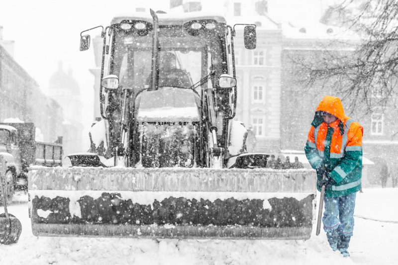 a worker shovelling snow beside a snow plough