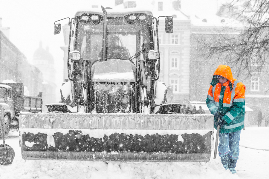 a worker shovelling snow beside a snow plough